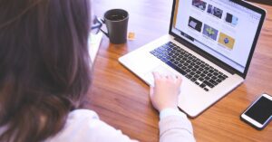 Person working on website branding in the UK at a wooden desk, with a laptop displaying branding visuals, a smartphone