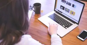 - brandyoucreative uk Person working on website branding in the UK at a wooden desk, with a laptop displaying branding visuals, a smartphone